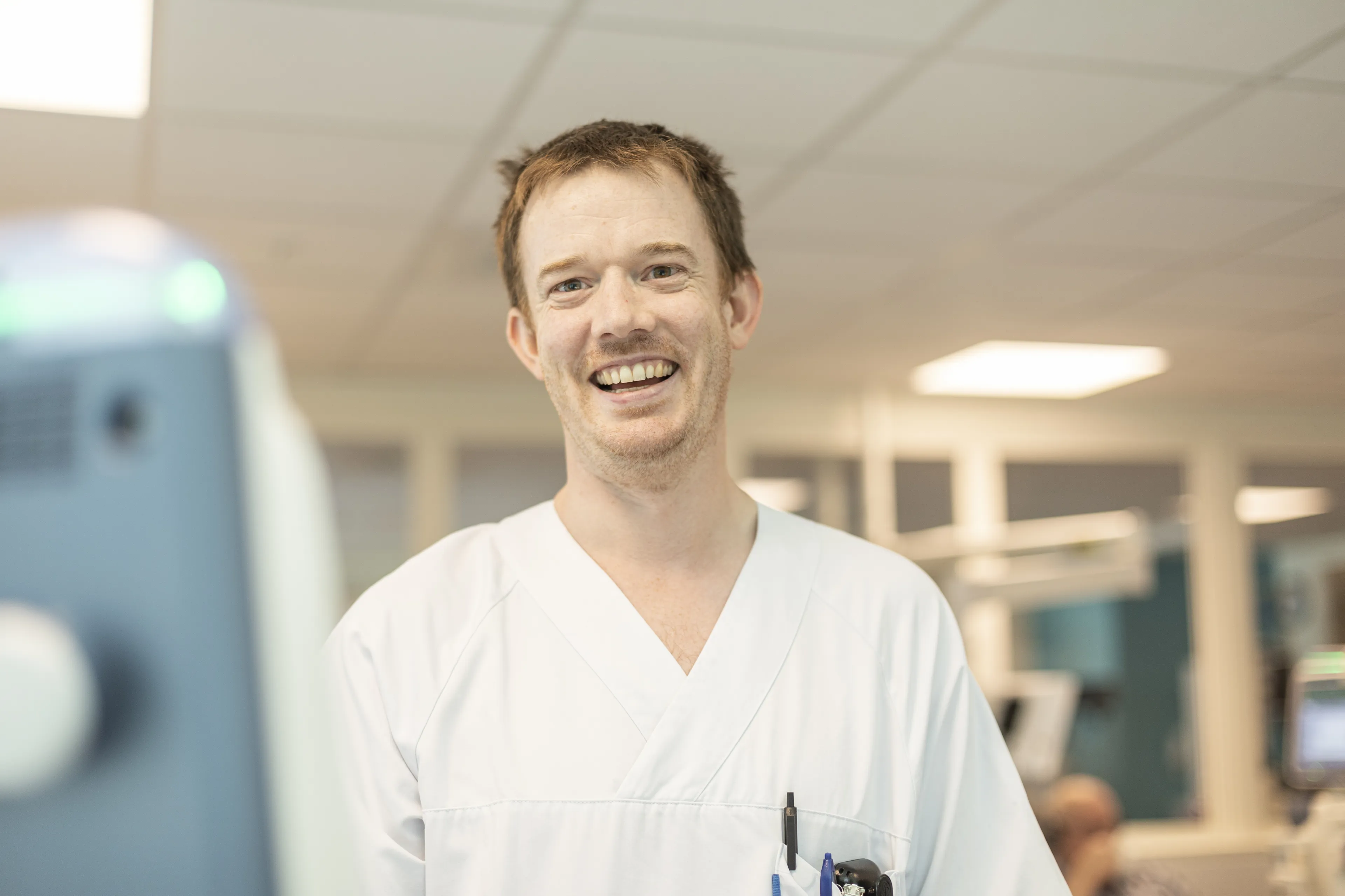 Person i hvitt sykehustøy smiler til kameraet. Foto.