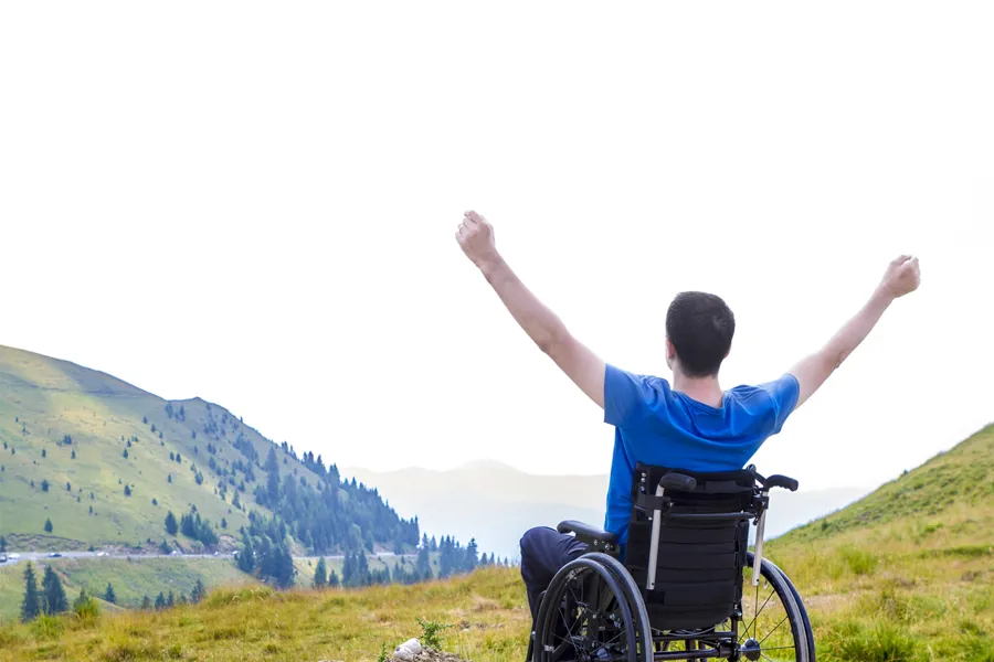 Mann i rullestol viser glede og optimisme ved å holde hendene i været. Foto.