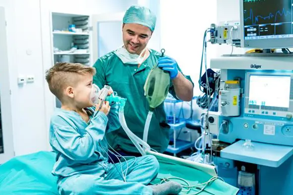 Elias er på operasjonsstuen. Han holder en maske over munn og nese. En lege hjelper til. Foto.