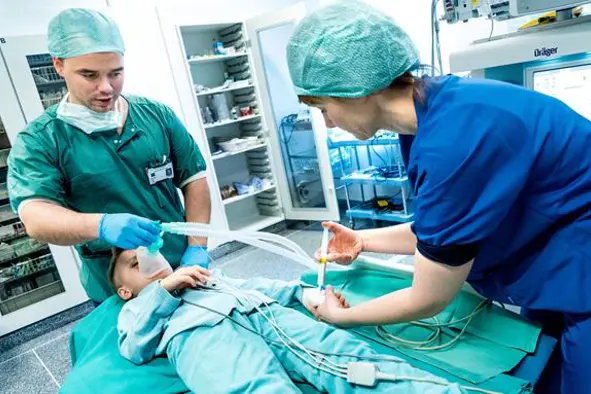 Elias ligger på operasjonsbenken. Sykepleieren sprøyter sovemedisin i veneflonen på hånden. Foto.